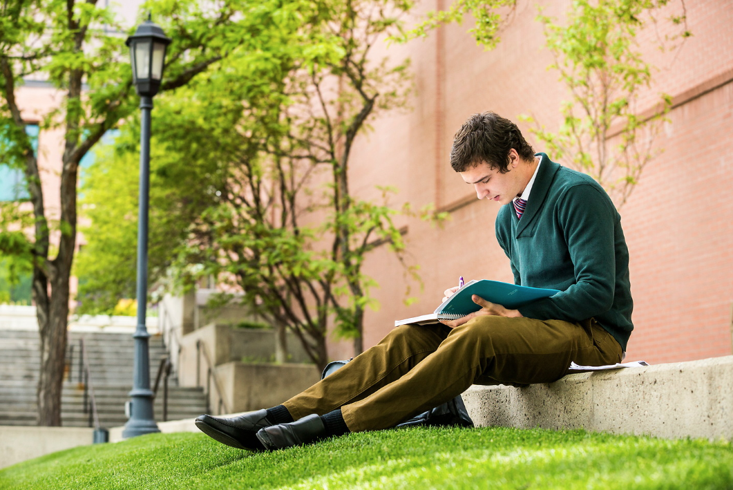 male sitting outside writing in notebook